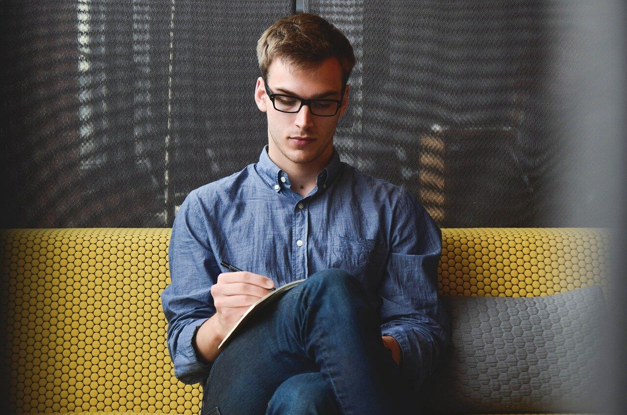 Young professional writing on a note while sitting on a sofa