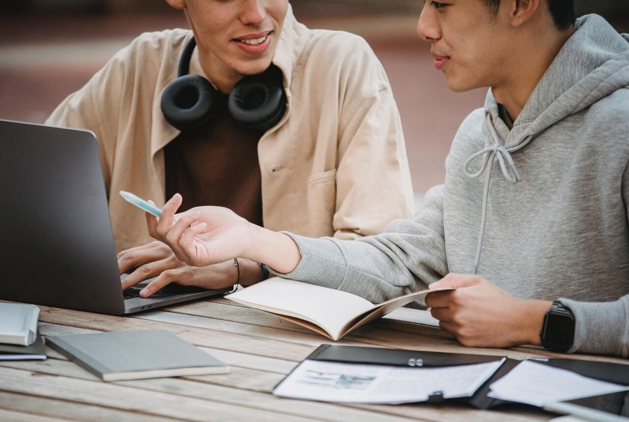 A-man-pointing-at-the-laptop-while-conversing-with-another-man