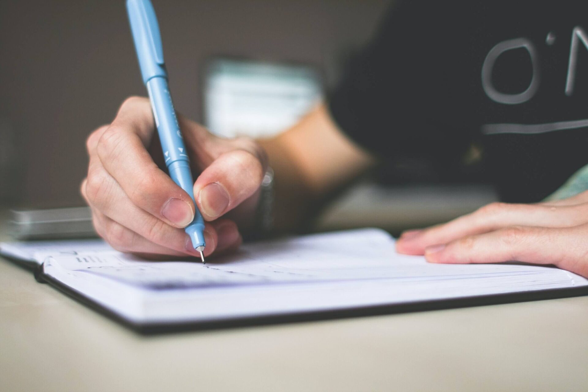 Person holding a pen writing in notebook