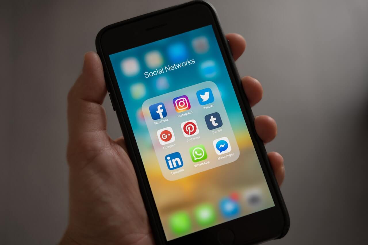 Person holding a phone displaying the logos of different social media platforms