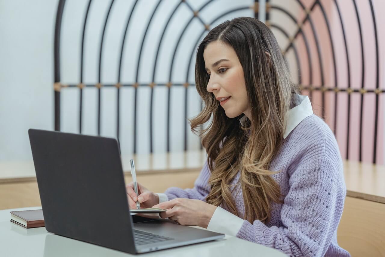 Woman writing in notebook and researching on laptop