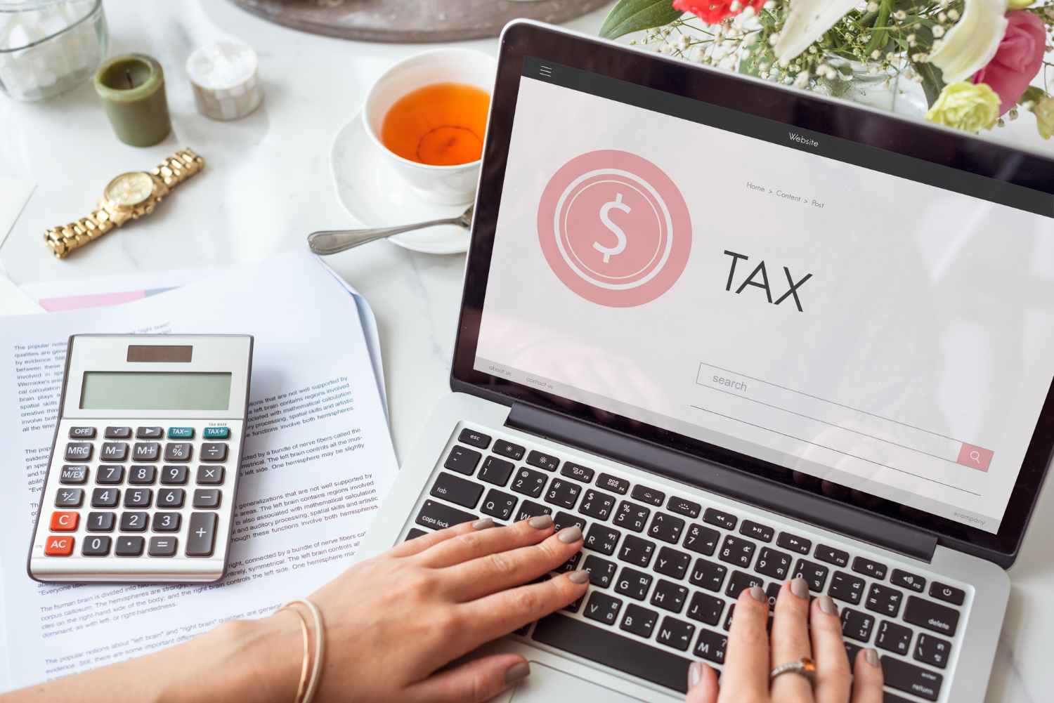 A person tying on a laptop with tax on the desktop