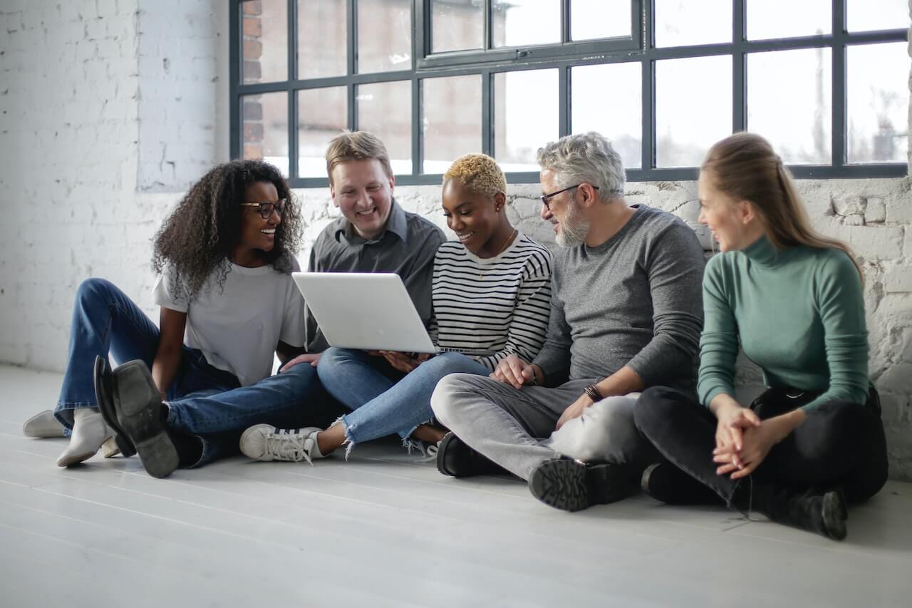 Cheerful colleagues with laptop sitting on floor