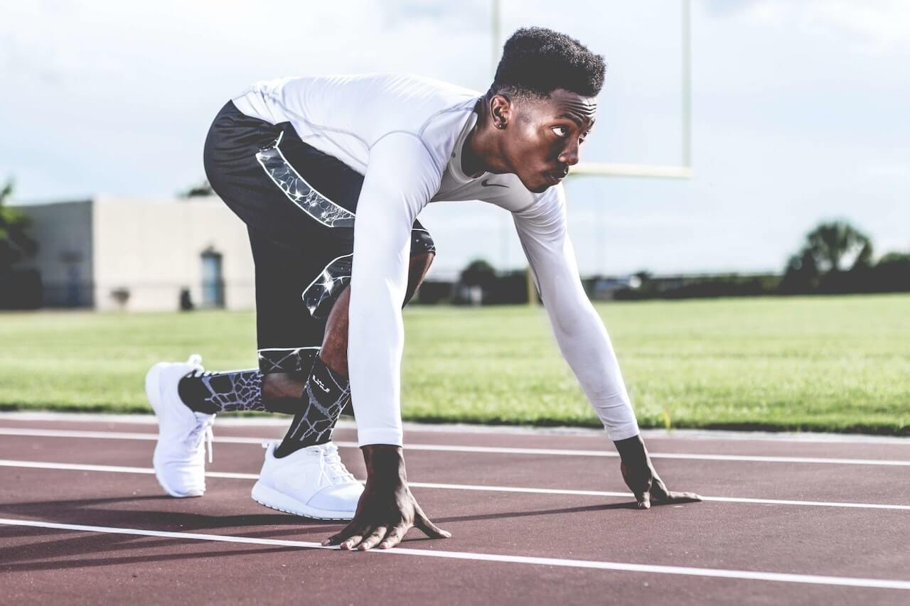 Man Wearing White Sweater and Black Shorts About to Run on a track