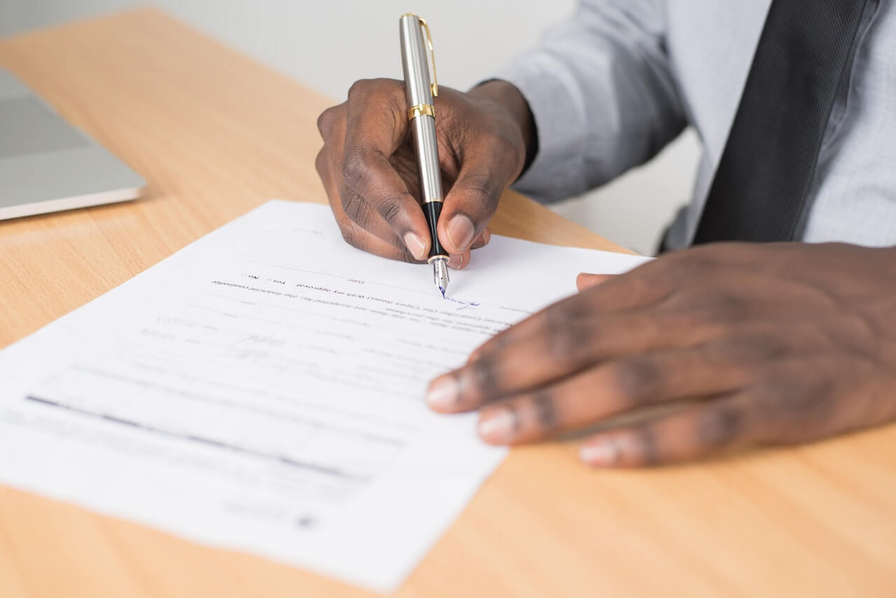 Person Holding Gray Twist Pen and White Paper on Brown Wooden Table